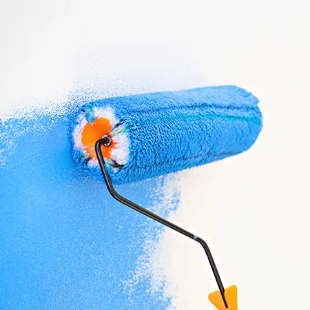 Målare använder en roller för att applicera blå målarfärg på vit vägg